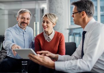 Happy mid adult couple using touchpad with their financial consultant in the office.